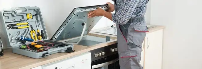 Cooktop repair technician lifting a built-in stovetop for service in Gilbert, AZ