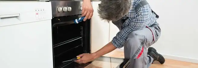 Oven repair technician inspecting and servicing an electric oven in Gilbert, AZ
