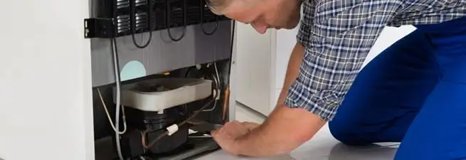 Refrigerator repair technician servicing the compressor and condenser area in Gilbert, AZ