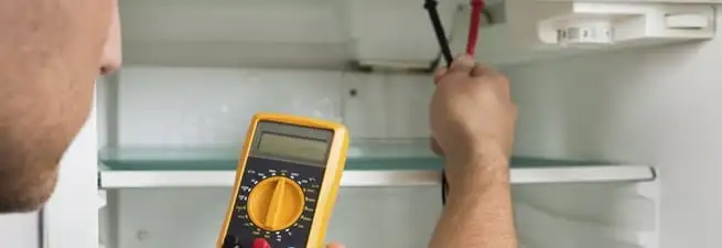 Refrigerator repair technician testing electrical components with a multimeter in Gilbert, AZ